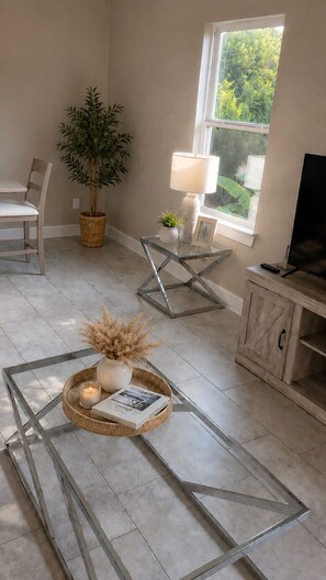 A living room with a glass coffee table, a chair, a potted plant, a lamp, and a television. -      The Haven House  A Peaceful Escape for Every Traveler (Houston)