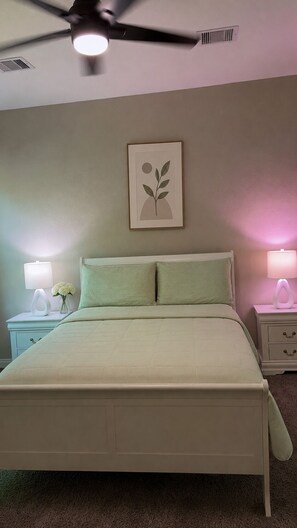A bedroom with a bed, a ceiling fan, bedside lamps, a wall-mounted picture, and a nightstand with a vase of flowers. -      The Haven House  A Peaceful Escape for Every Traveler (Houston)