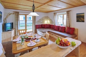 A cozy room with a wooden ceiling, a dining table set with plates, cups, and a fruit bowl, and a sofa with red cushions. - Brauneck holiday home (Lenggries)
