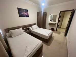 Quarto de hotel com duas camas, guarda-roupa de madeira, espelho e uma obra de arte com vista para a cidade.