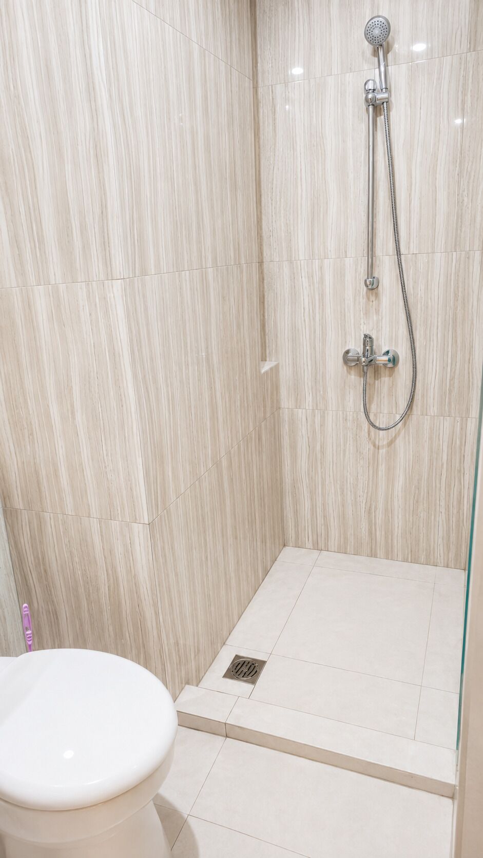 A bathroom with a shower, toilet, and a tiled floor.
