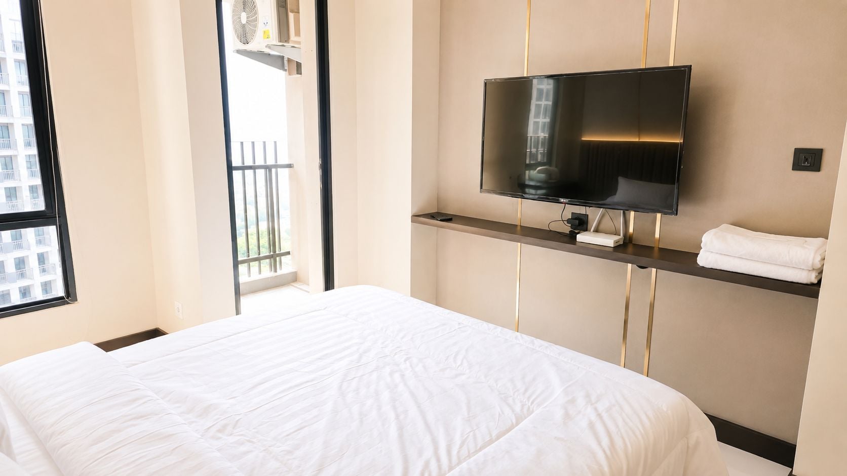 Ett hotellrum med en säng, en väggmonterad tv och ett fönster med utsikt över en byggnad.