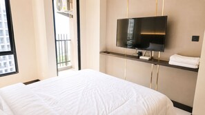 A hotel room with a bed, a mounted television, and a window with a view of a building.