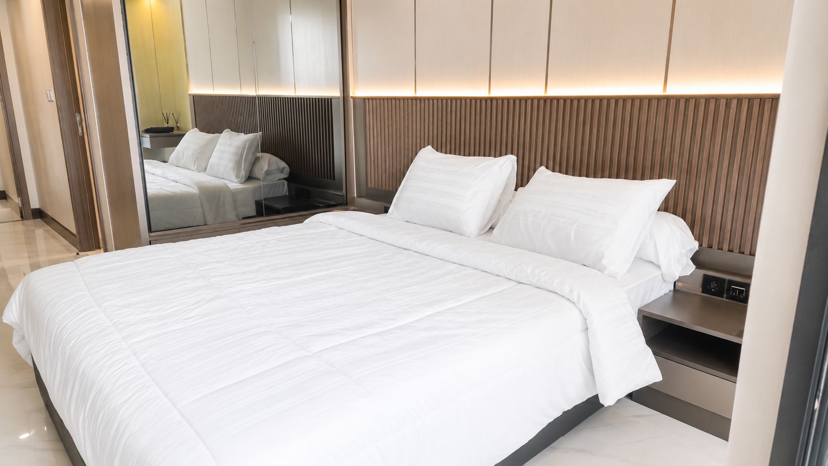 Una habitación de hotel moderna con una cama grande, una mesita de noche con un reloj y un espejo.