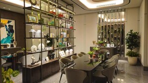A modern dining area with a long table, chairs, and a bookshelf filled with decorative items. - Apartmen Pakuwon by Fiola Homes (Jawa Barat)