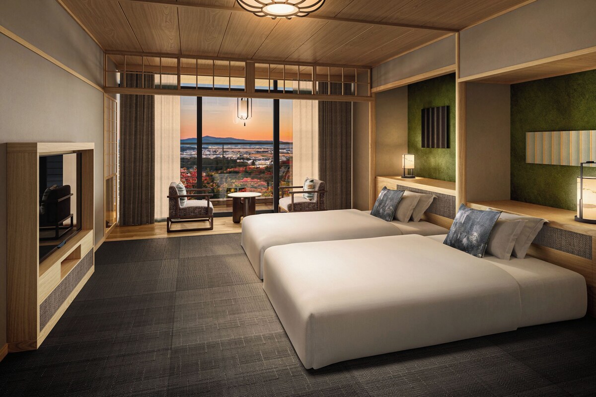 Habitació d'hotel amb una finestra gran, dues lliteres, televisió i vista a la ciutat.
