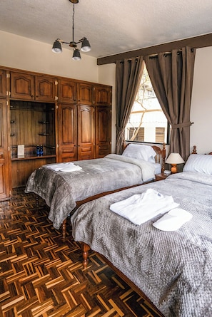 A bedroom with two beds, wooden wardrobe, and a herringbone-patterned floor. - Casa BuenaVida  (Quito)