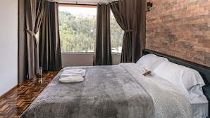 A bedroom with a large window, a wooden floor, a bed with white linens, and a brick wall. - Casa BuenaVida  (Quito)