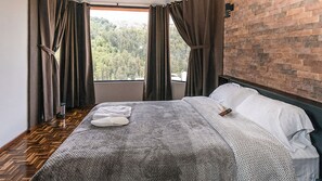 A bedroom with a large window, a wooden floor, a bed with white linens, and a brick wall. - Casa BuenaVida (Quito)