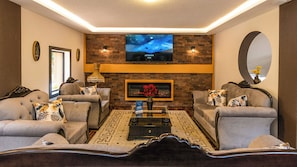 A living room with a fireplace, sofas, a coffee table, and a flat-screen TV mounted on a brick wall. - Casa BuenaVida (Quito)