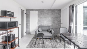 A modern living room with a grey sofa, a dining table, and a kitchen area with appliances. - ASTAGE CHITOSE SUEHIRO 103 (Chitose)