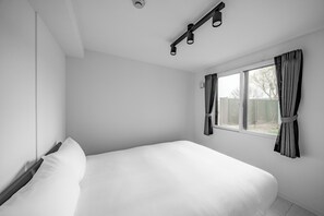 Un dormitorio minimalista con una cama grande, una ventana con cortinas y una lámpara en el techo.