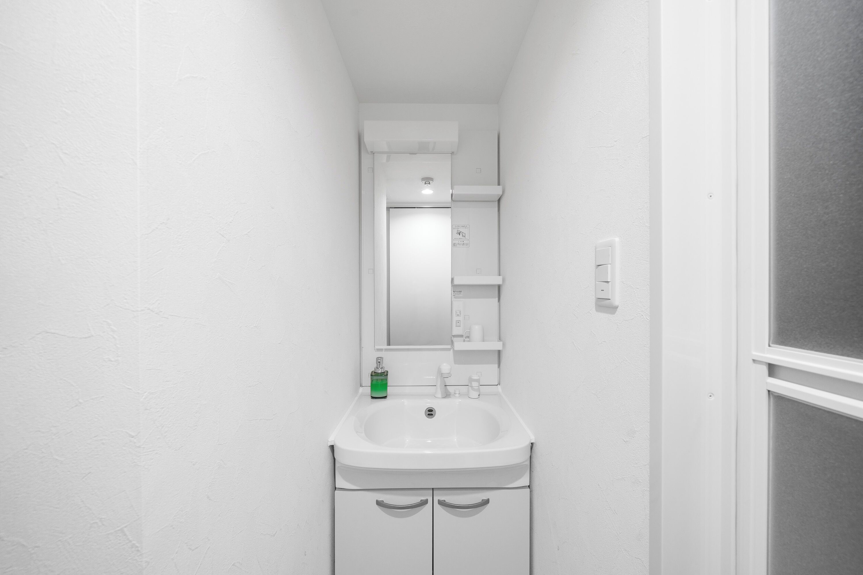 Een smalle badkamer met een wit wastafel, spiegel en een klein schapje boven de spiegel.