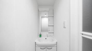 Een smalle badkamer met een wit wastafel, spiegel en een klein schapje boven de spiegel.