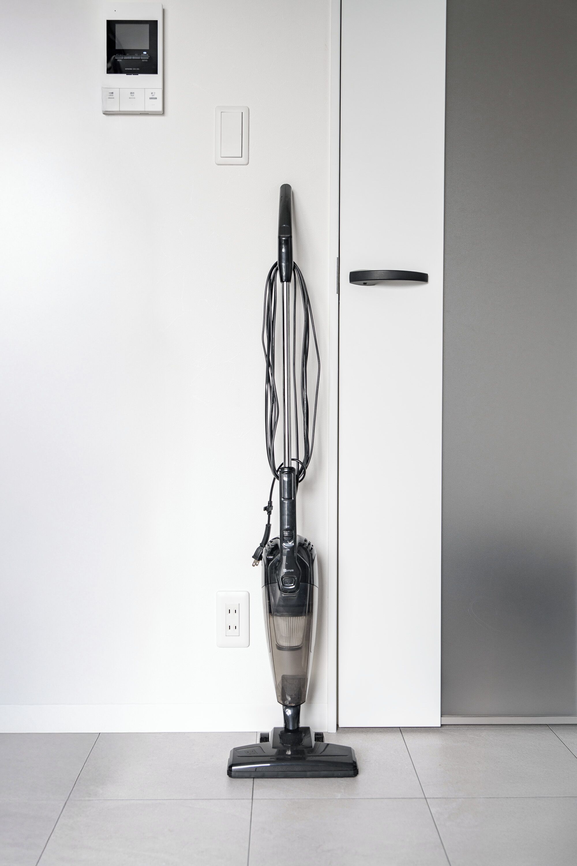 A vacuum cleaner in a room with a white door, a power outlet, and a thermostat on the wall.