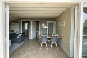 Et åbent opholdsområde med spisebord, stole, sofa og et køkken i baggrunden.