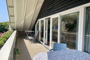 A balcony with a table and chairs, a green bottle, and a view of the street and greenery. - Prinsepark 1st floor (Domburg)