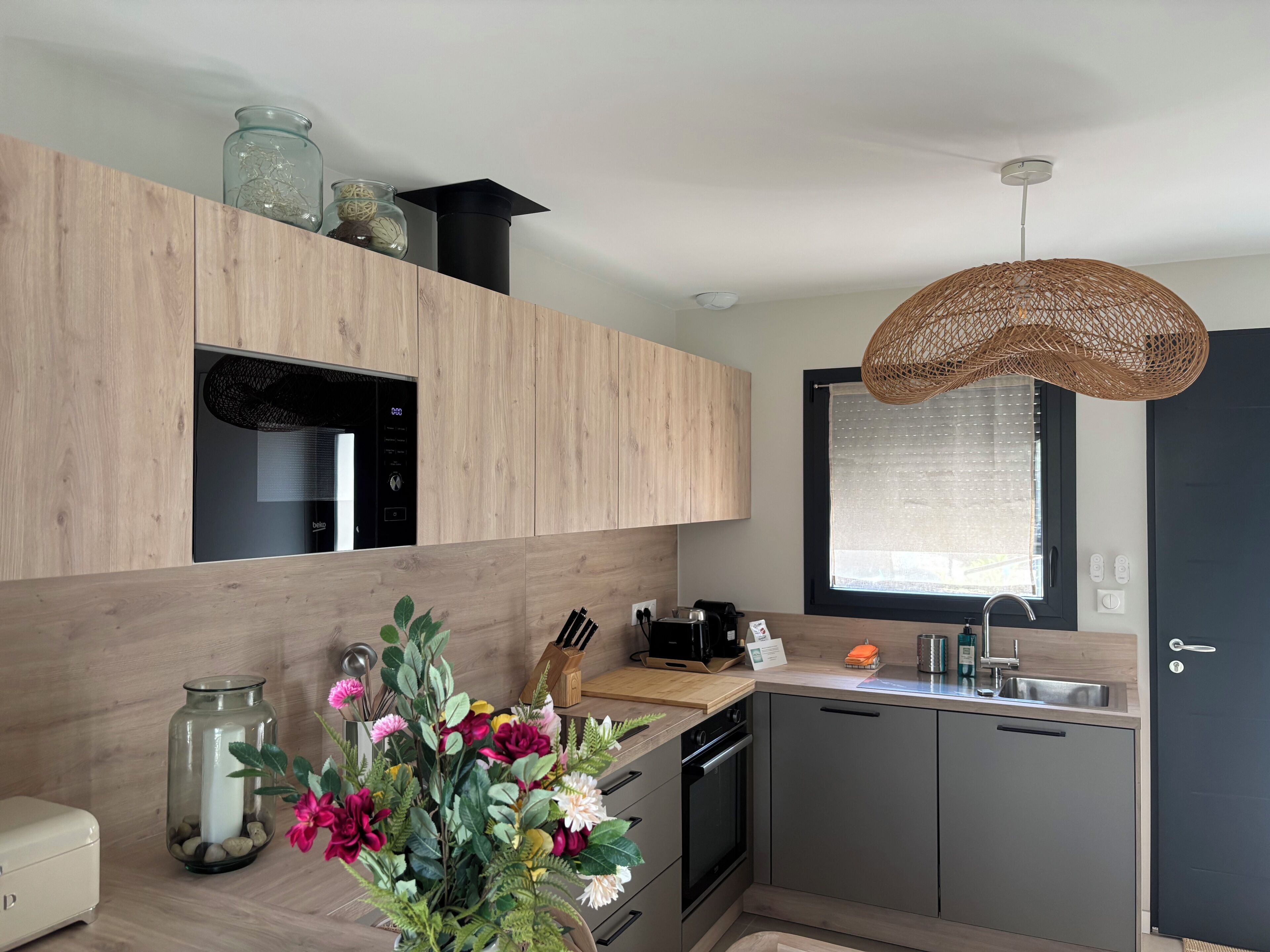 A modern kitchen with wooden cabinets, a built-in oven, a sink, and a decorative vase with flowers.