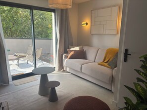 A modern living room with a sofa, a small round table, and a glass door leading to an outdoor patio with chairs.