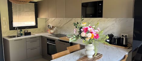 A modern kitchen with a marble countertop, a dining table, and a vase of flowers.