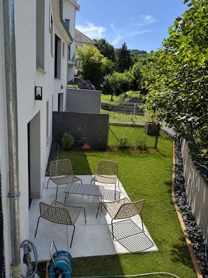 Eine Terrasse mit Tisch und Stühlen, einem Gartenschlauch und einem Rasenstück, das von einem Zaun begrenzt wird.