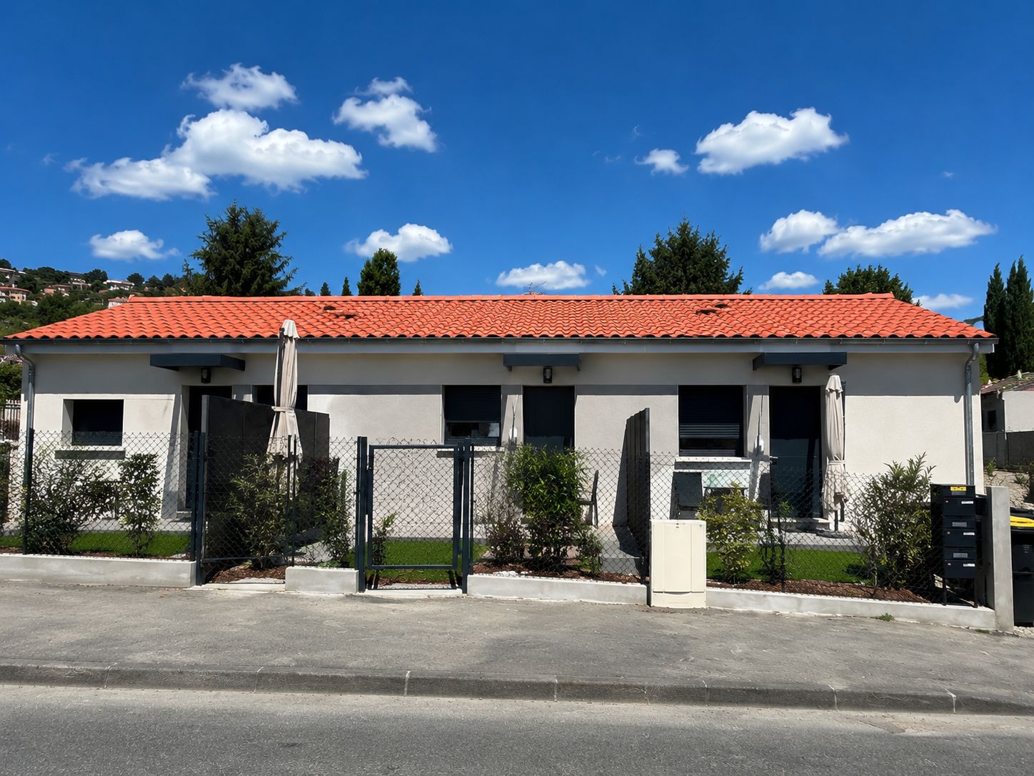 A two-story building with a red-tiled roof, a gated entrance, and a small front yard.
