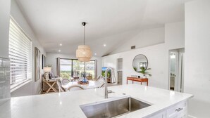 A modern kitchen with a large island, stainless steel sink, and a dining area with wicker chairs. - PGA National Cottage | Pool, Patio & Golf (Palm Beach Gardens)