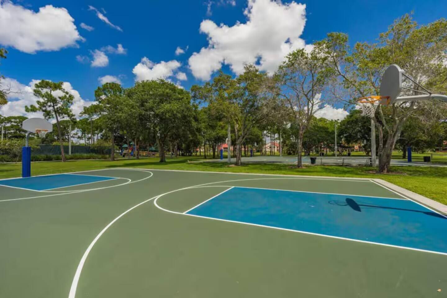A basketball court with two hoops, surrounded by trees and a clear sky.