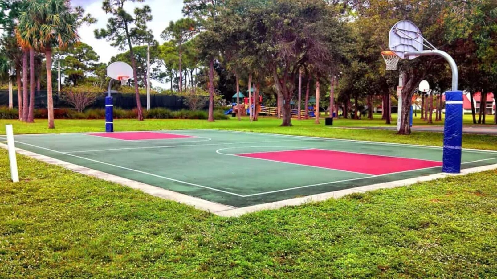 An outdoor basketball court with a green playing surface, red areas, and two basketball hoops.