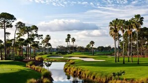 A golf course with a pond, palm trees, and a clear sky. - PGA National Cottage | Pool, Patio & Golf (Palm Beach Gardens)