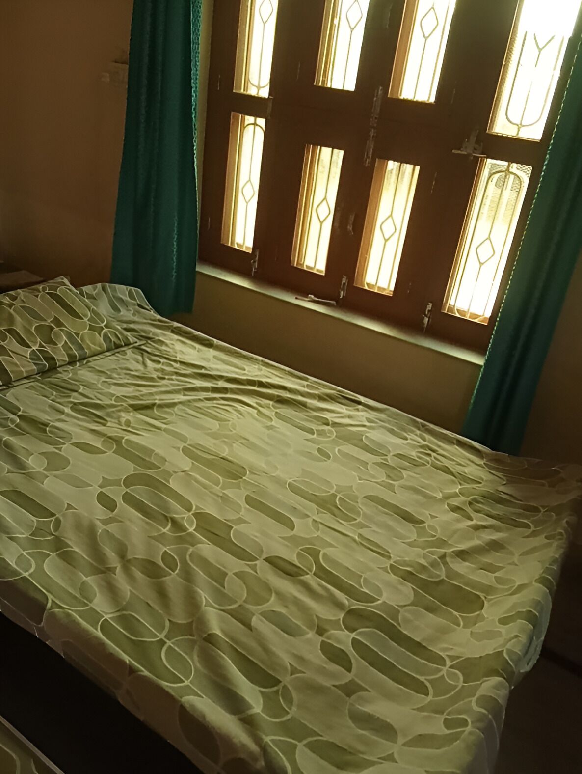 Un llit amb un estenat estampat, una finestra amb vidres decoratius i cortines color aquamarina.