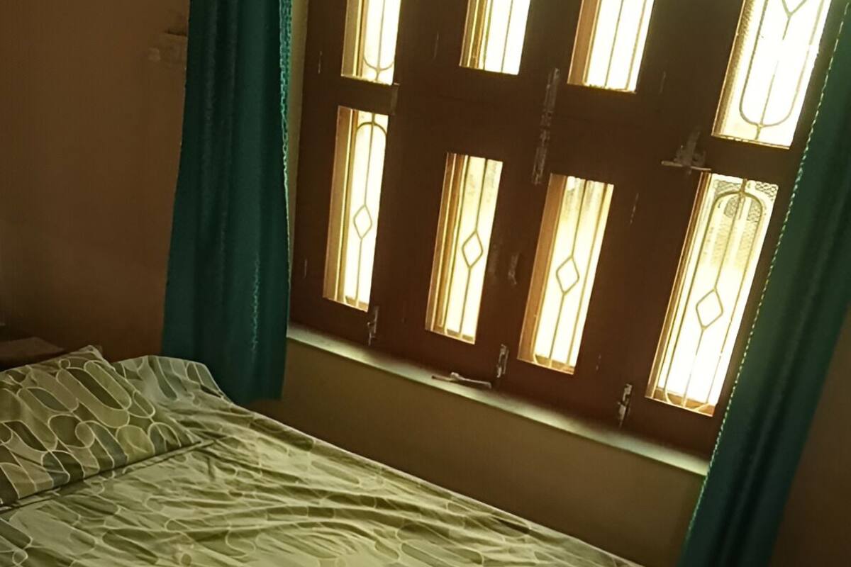 A bed with a patterned bedspread, a window with decorative glass panes, and teal curtains.