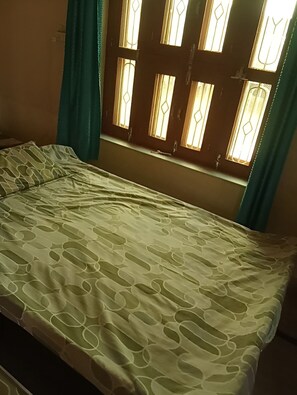 Un llit amb un estenat estampat, una finestra amb vidres decoratius i cortines color aquamarina.