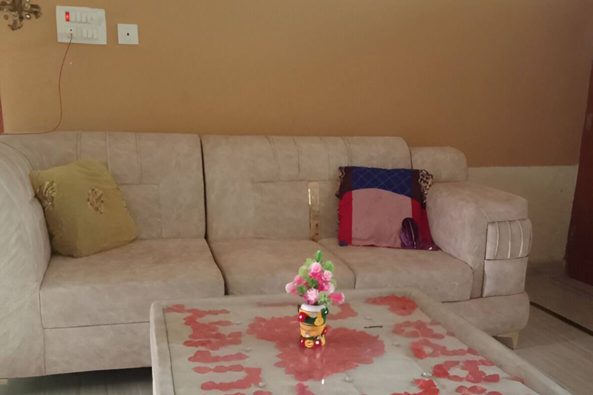 A living room with a beige sofa, a glass coffee table with rose petals, a decorative vase, and a wall socket.