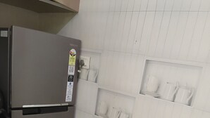 Una cocina con un refrigerador de acero inoxidable, paredes de azulejos blancos y estantes empotrados para vajilla.