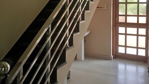 Una escalera con barandilla de vidrio que lleva a una plataforma, una puerta blanca con paneles de vidrio y vistas a zonas verdes.