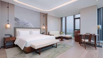 A modern hotel room with a large bed, a seating area, and a view of the city.