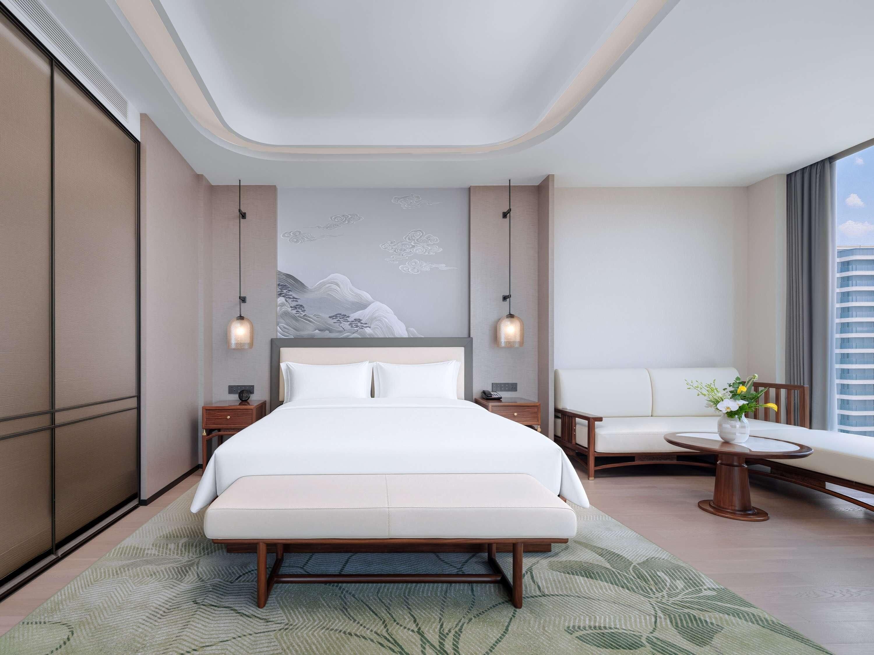 Ein modernes Hotelzimmer mit einem großen Bett, einer Sitzecke mit Tisch und Blick auf die Stadt.