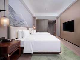 Una habitación de hotel con una cama grande, un escritorio, una silla, un televisor y un cuadro en la pared.
