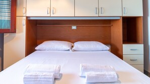 A hotel room with a bed, two pillows, a wooden headboard, a nightstand, and a drawer. - Casa Libeccio - Pistis - wifi - Pet Friendly (Arbus)