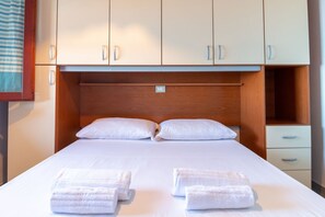 A hotel room with a bed, two pillows, a wooden headboard, a nightstand, and a drawer. - Casa Libeccio - Pistis - wifi - Pet Friendly (Arbus)