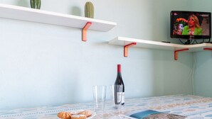 A room with a table, two white shelves with red brackets, a television, a bottle of wine, two glasses, and a plate with cookies. - Casa Libeccio - Pistis - wifi - Pet Friendly (Arbus)