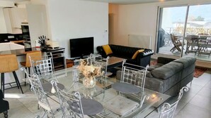 A modern living room with a glass dining table, a sofa, and a large window offering a view. - T3 Dolce Bateau, a 5-minute walk from the 3*-rated lake (Aix-les-Bains)