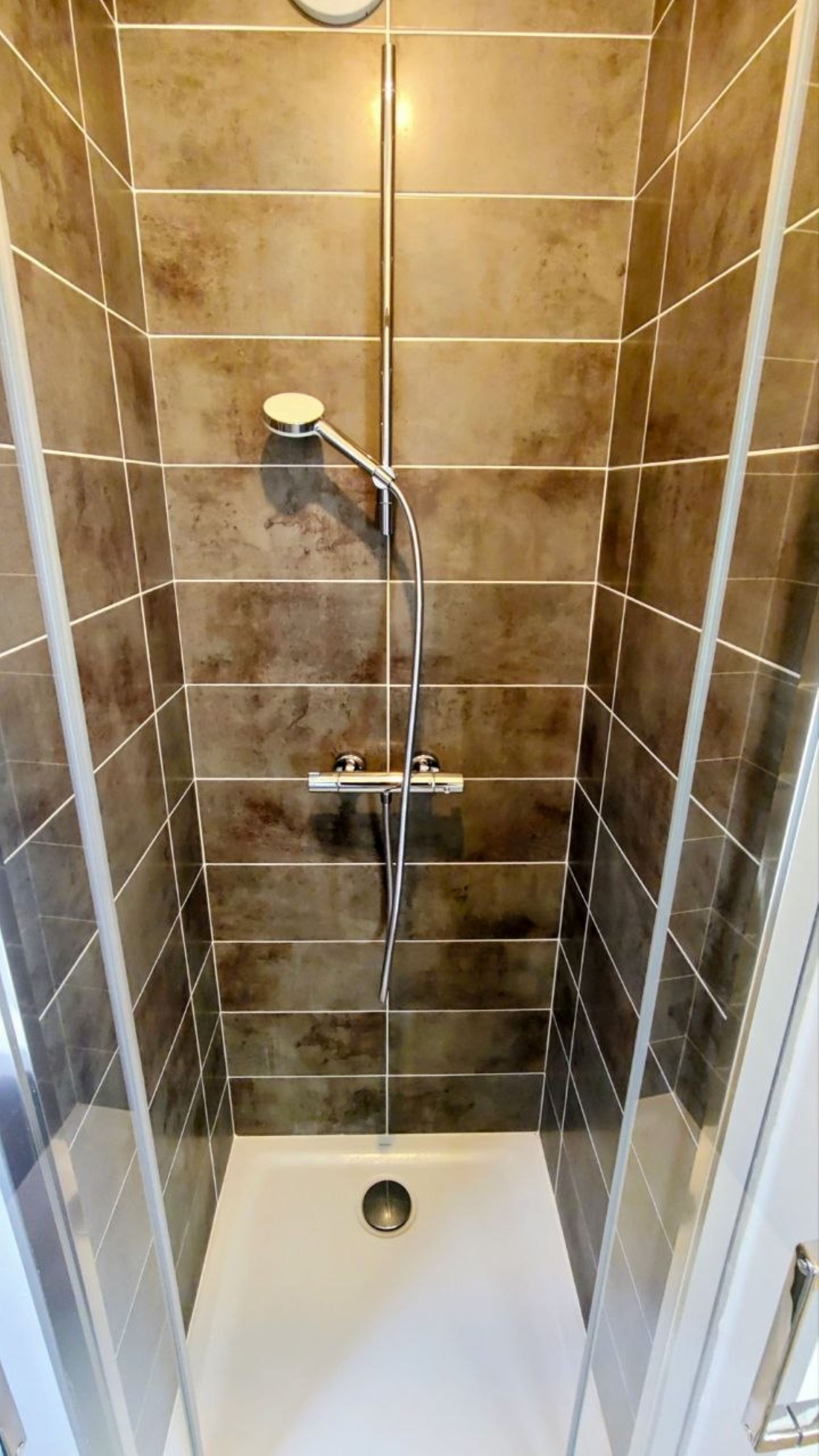 A shower with a handheld showerhead and a wall-mounted control panel.