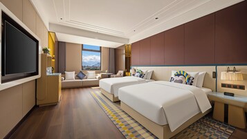 A hotel room with a large flat-screen TV, two beds, a sofa, a small table, and a view of the city.