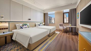 Une chambre d’hôtel avec deux lits, un bureau, une chaise, une télévision et une fenêtre donnant sur des immeubles.
