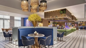 A modern hotel lobby with a seating area, a bar, and a decorative plant arrangement.