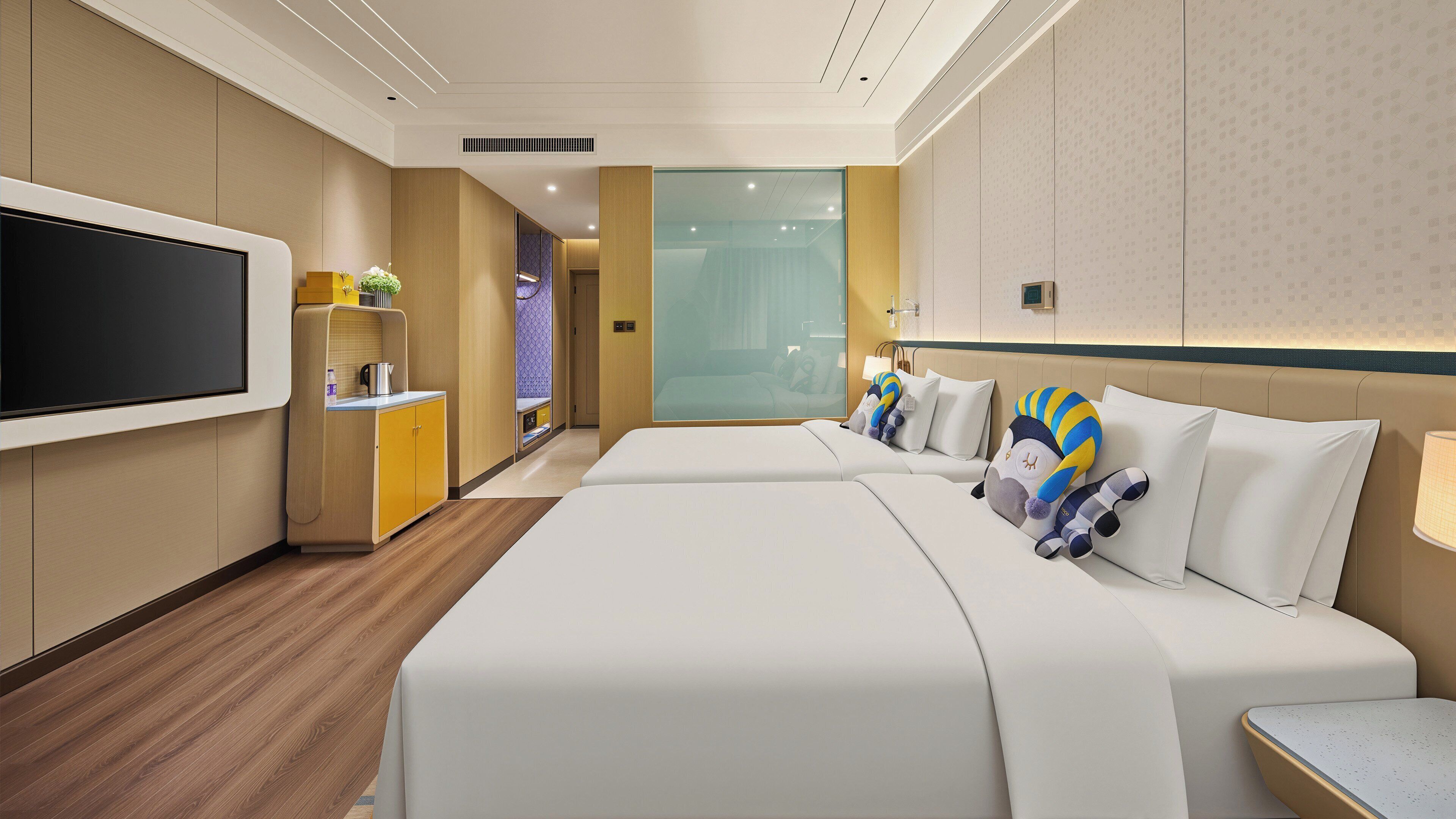 A hotel room with a large flat-screen TV, a minibar, a bed with decorative pillows, and a view of the hallway.
