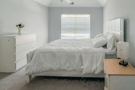 A bedroom with a bed, a dresser, a nightstand, a window with blinds, and a ceiling fan.. Nyakio Suite - Chesapeake