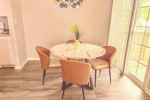 Un coin repas comprenant une table ronde, quatre chaises, un vase avec des fleurs et une fenêtre avec des stores.